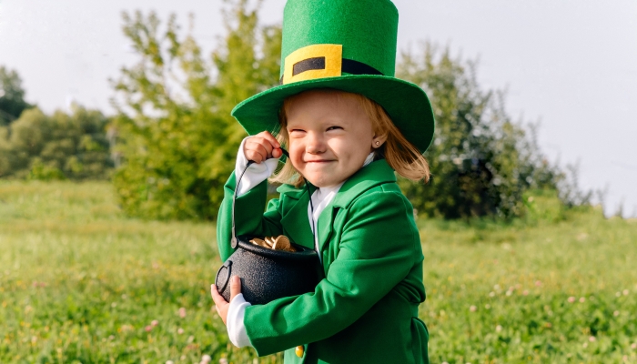 Portrait of a beautiful little girl in a leprechaun costume who holds a pot of gold coins in her hands.