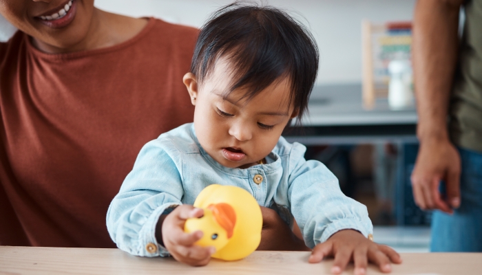 Sleeping, disability and baby with down syndrome after playing with toy asleep on his mothers lap in family home.