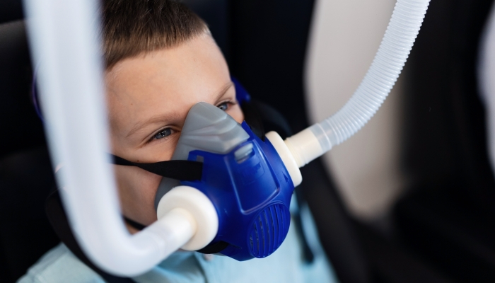 Small kid breathing through oxygen mask while having therapy in hyperbaric chamber.