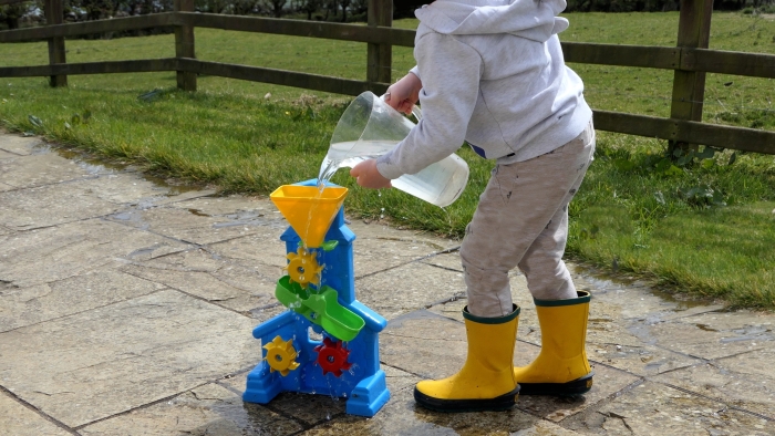 Small redhead boy playing and puddling in water in the garden.