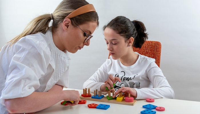 The girl sorts geometric shapes and is helped by the teacher.