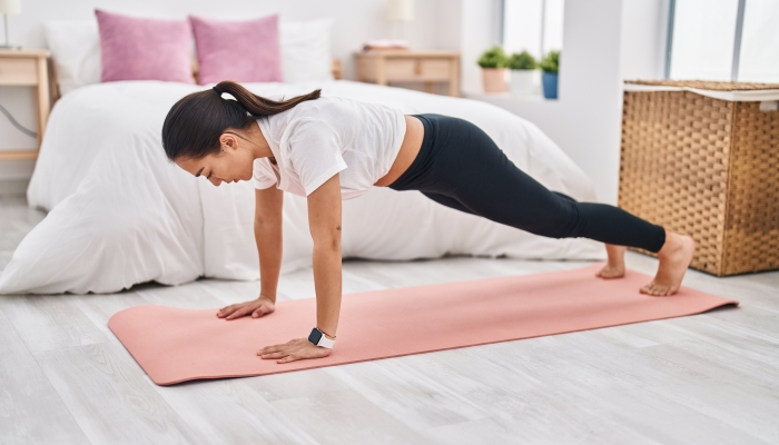 Young hispanic woman training push up at bedroom.