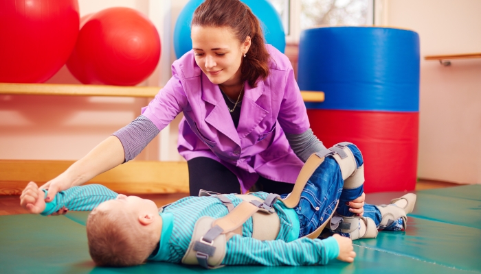 Cute kid with disability has musculoskeletal therapy by doing exercises in body fixing belts.