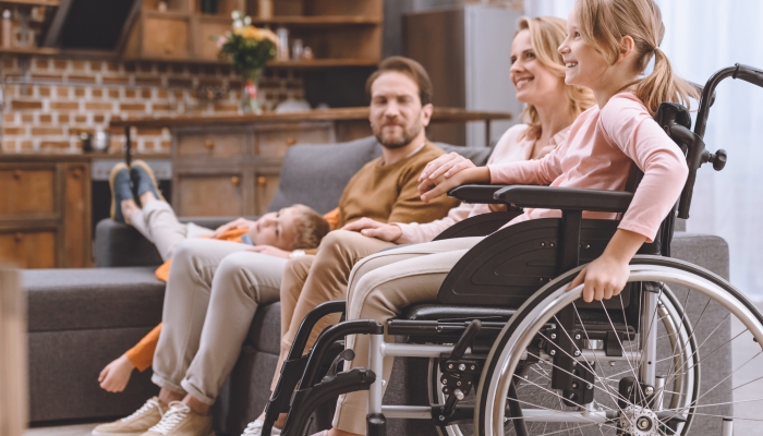 Happy family with disabled little daughter in wheelchair spending time together at home.