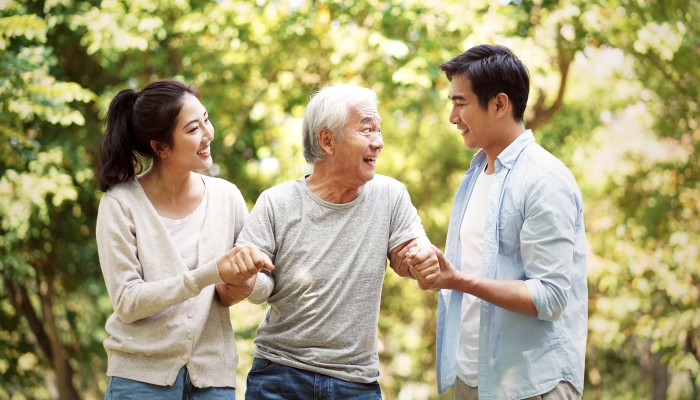Young asian man and woman helping senior man stand up and walk.