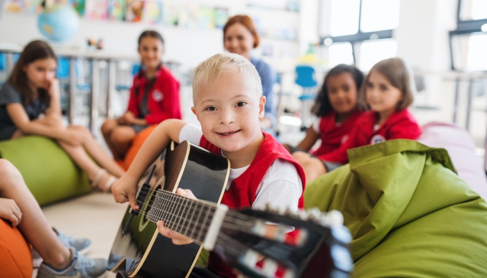 A down-syndrome boy with school kids and teacher sitting in class, playing guitar.