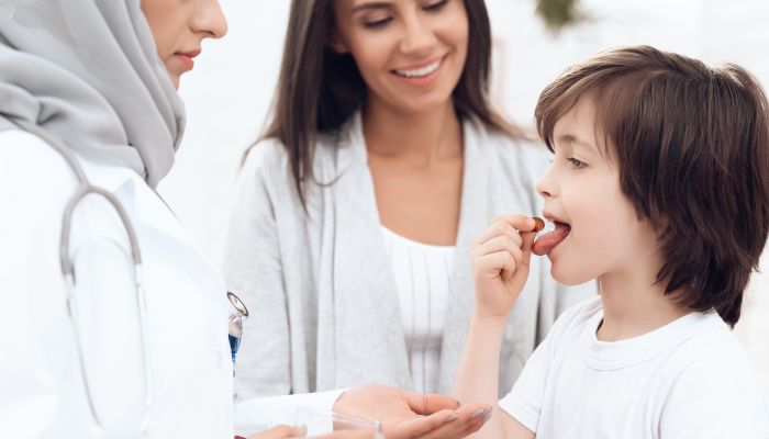 A female doctor in hijab gives the boy a pill for the throat.