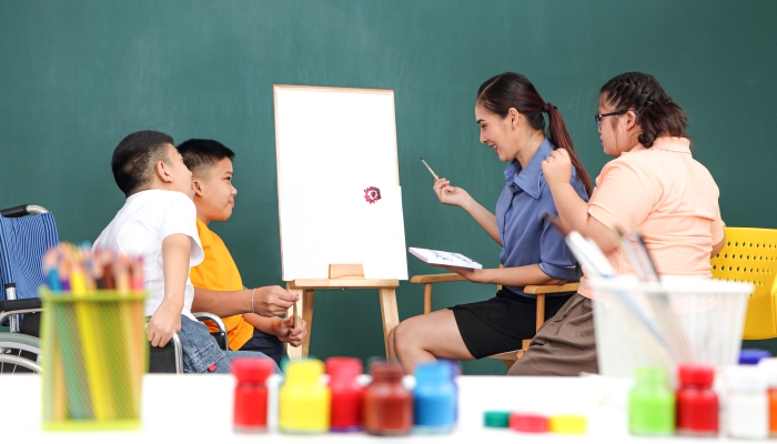 A group of young girls with disabilities and autism is training their hand and finger muscles by drawing and painting with water.