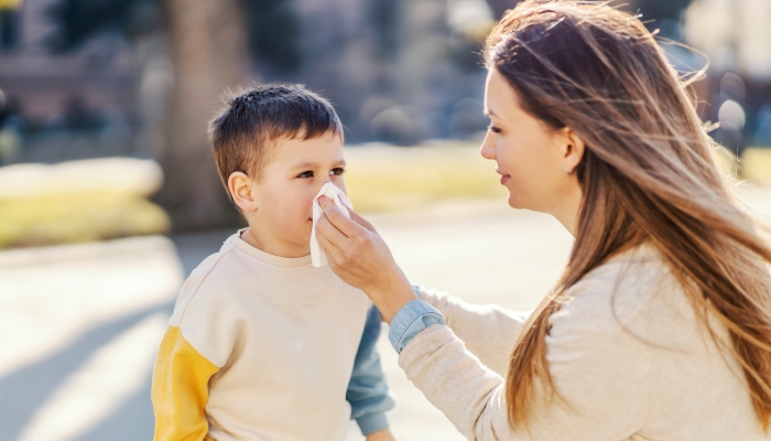 A mother helping son to blow a nose in a park.