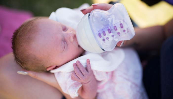 A tiny premature baby girl being fed by bottle by her mother.