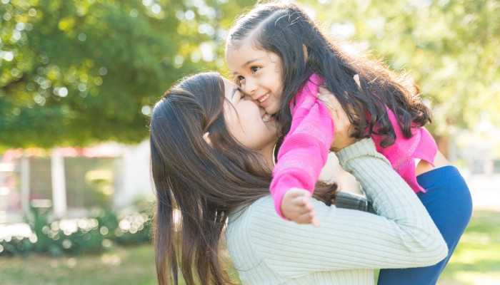 Affectionate Mother Carrying Adorable Daughter At Park During Weekend.