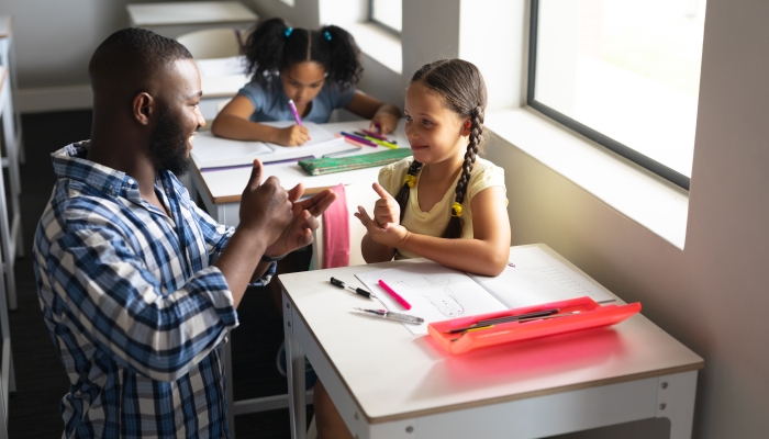 African american young male teacher communicating in sign language with caucasian elementary girl.