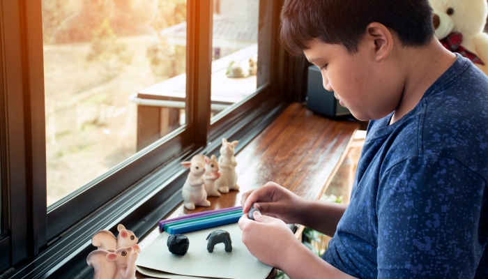 An autistic boy molding different shapes of colored plasticine prepared by parents at home.