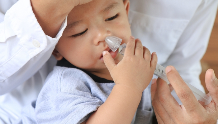 Asian father rinsing baby's stuffy nose using a syringe of saline water.