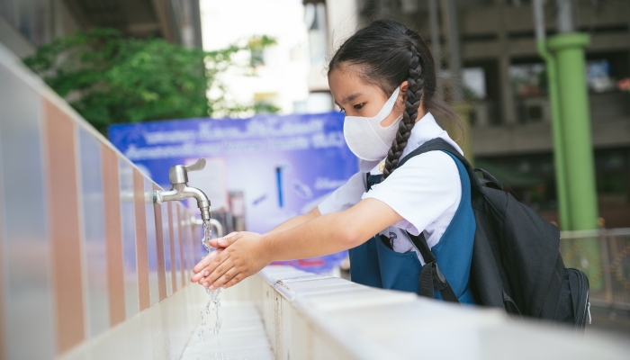 Asian student washing hands at the outdoor wash basin in the school.
