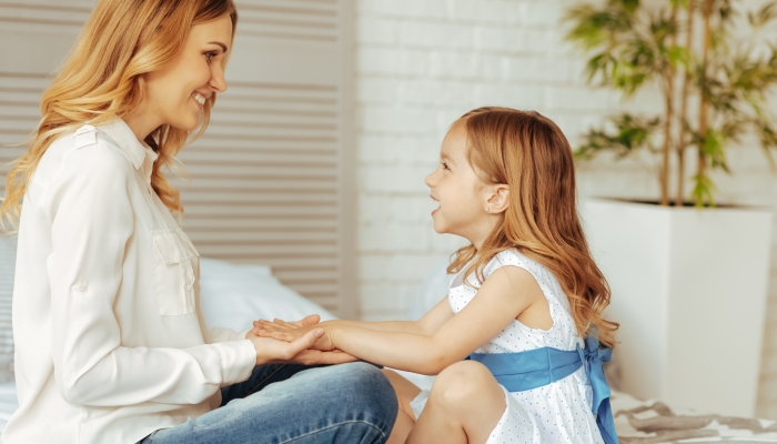 Beautiful cheerful blonde woman looking at her daughter and smiling while holding her hands.
