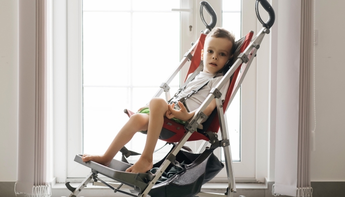 Boy with with Cerebral Palsy in special chair going outside by the door.