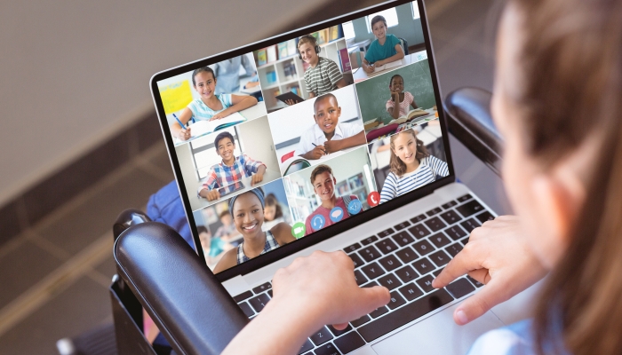 Caucasian girl with disability attending online class on laptop while sitting on wheelchair at home.