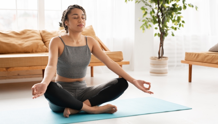 Charming young african woman meditating on the floor at home.