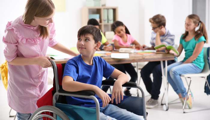 Girl helping boy in wheelchair at school.