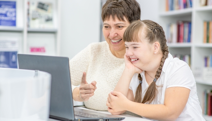 Grand mother and smiling grand daughter with down syndrome use a laptop.