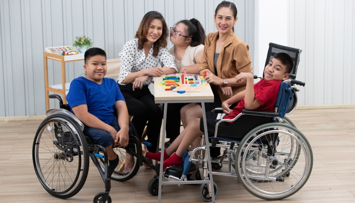 Group of special students in classroom, a down syndrome girl, two handicapped boys and cute Asian teacher playing toy and game together.