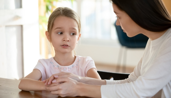 Head shot unhappy small child girl sitting at table with worrying mother, sharing school problems.