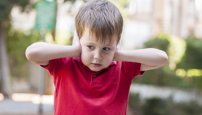 Little Caucasian boy in red polo shirt closing ears with his hands.