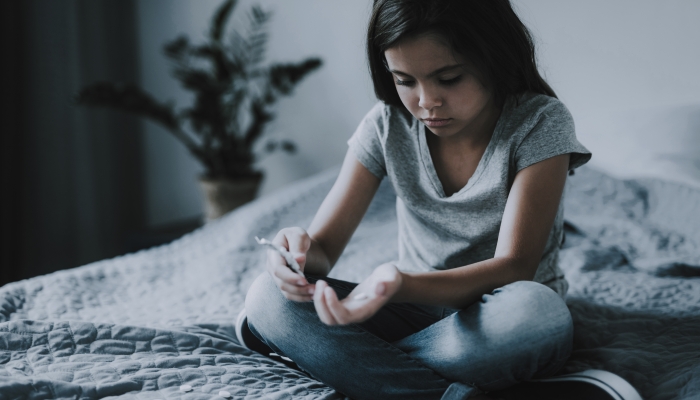 Little Girl Sits on Bed with Scattered Pills.