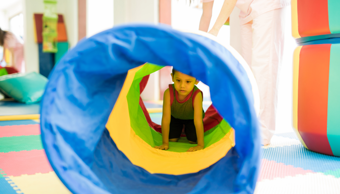 Little kid playing and crawling through a tunnel in an obstacle course.