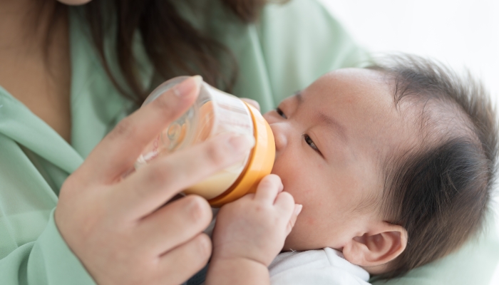 Mother carrying and feeding newborn baby with milk bottle.