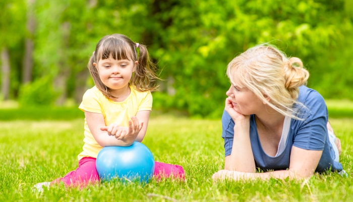 Mother talks with little girl with syndrome down in a summer park.