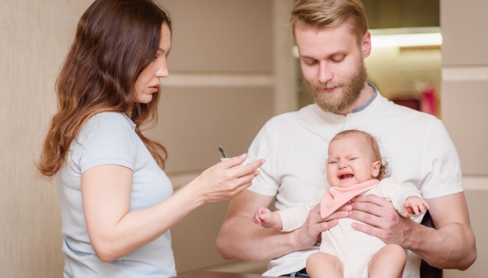 Parents feed their naughty daughter who refuses to eat fruit puree.