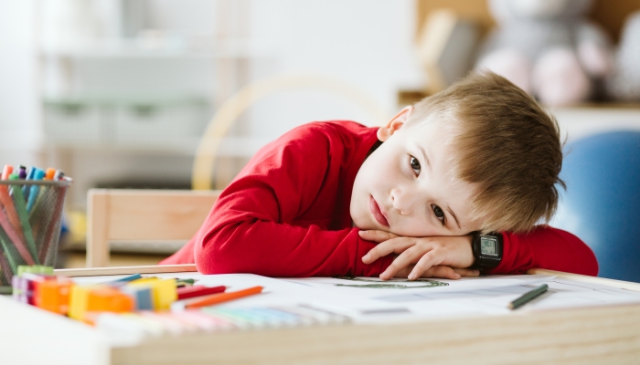 Sad little boy in red sweater feeling lonely and lying on a table.