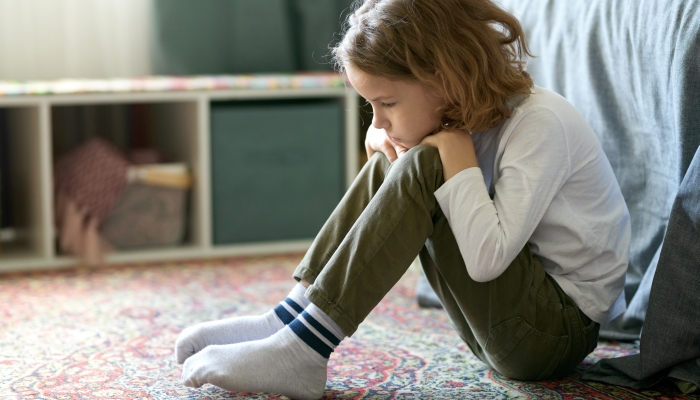 Sad little boy sitting on floor in his bedroom and feeling lonely.