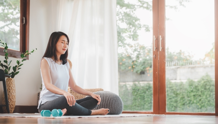 Shot of attractive healthy Asian woman doing meditation at home in living room.