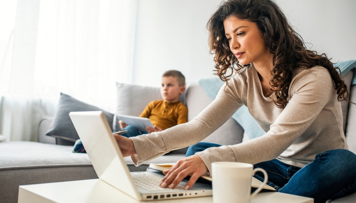 Smiling mom working at home with her child on the sofa while writing an email.