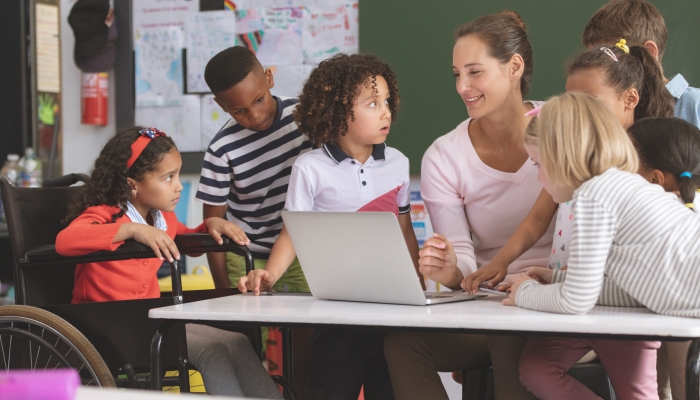 Teacher and students discussing over laptop in classroom at school.