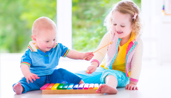 Two little children - cute curly toddler girl and a funny baby boy, brother and sister playing music.