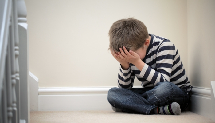 Upset problem child with head in hands sitting on staircase concept for bullying, depression stress or frustration.