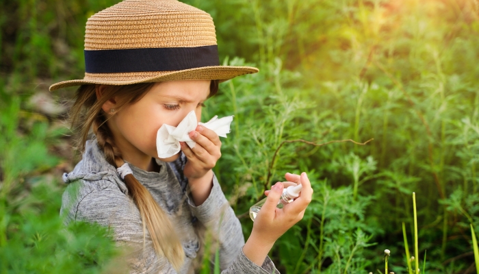 Young girl blowing nose with nasal sprays and other medication in foreground - allergy concept.