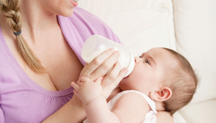 Young mother at home feeding their new baby girl with a milk bottle.