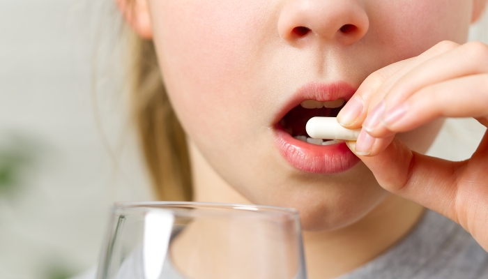 Girl eating white pills medicine tablet and drink glass of water.