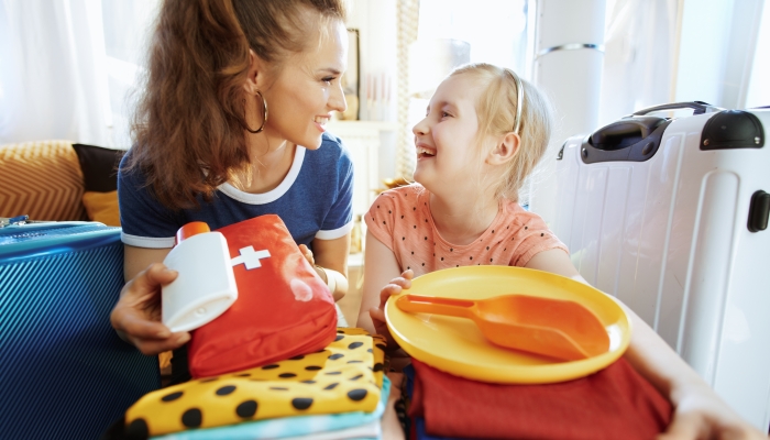 happy young mother and child travellers with open suitcase suitcase ready for resort at modern home in sunny summer day.