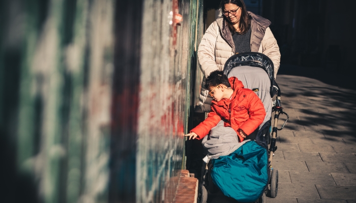 The mother takes her son with multiple disabilities to walk on the street in winter with an adapted stroller.