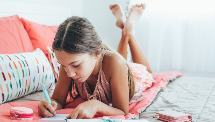 10-12 years old pre teen girl writing diary in pink bedroom.