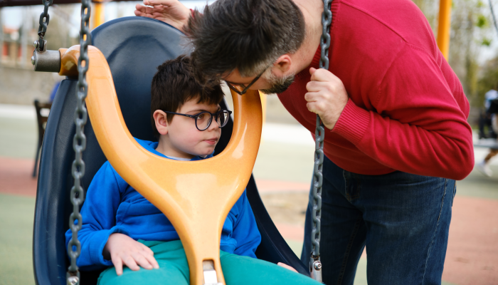 A disabled boy and his father enjoy playing in the park playground with a special needs swing.