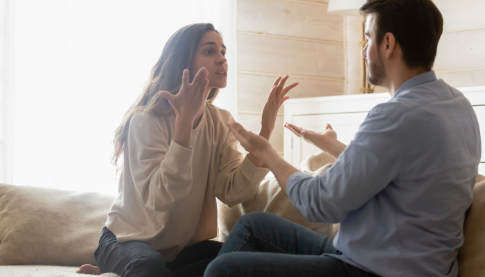 Angry young couple sit on couch in living room having family fight.