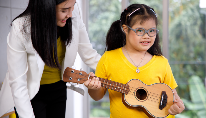 Asian teacher teach ukulele to girl with Down's syndrome.