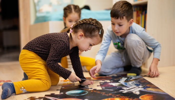 Children connecting jigsaw puzzle pieces in a kids room on floor at home.